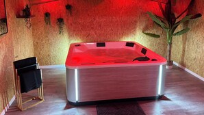 Une salle de bain moderne avec un plafond en bois, un jacuzzi éclairé en rouge, un porte-serviettes noir et une grande plante en pot.
