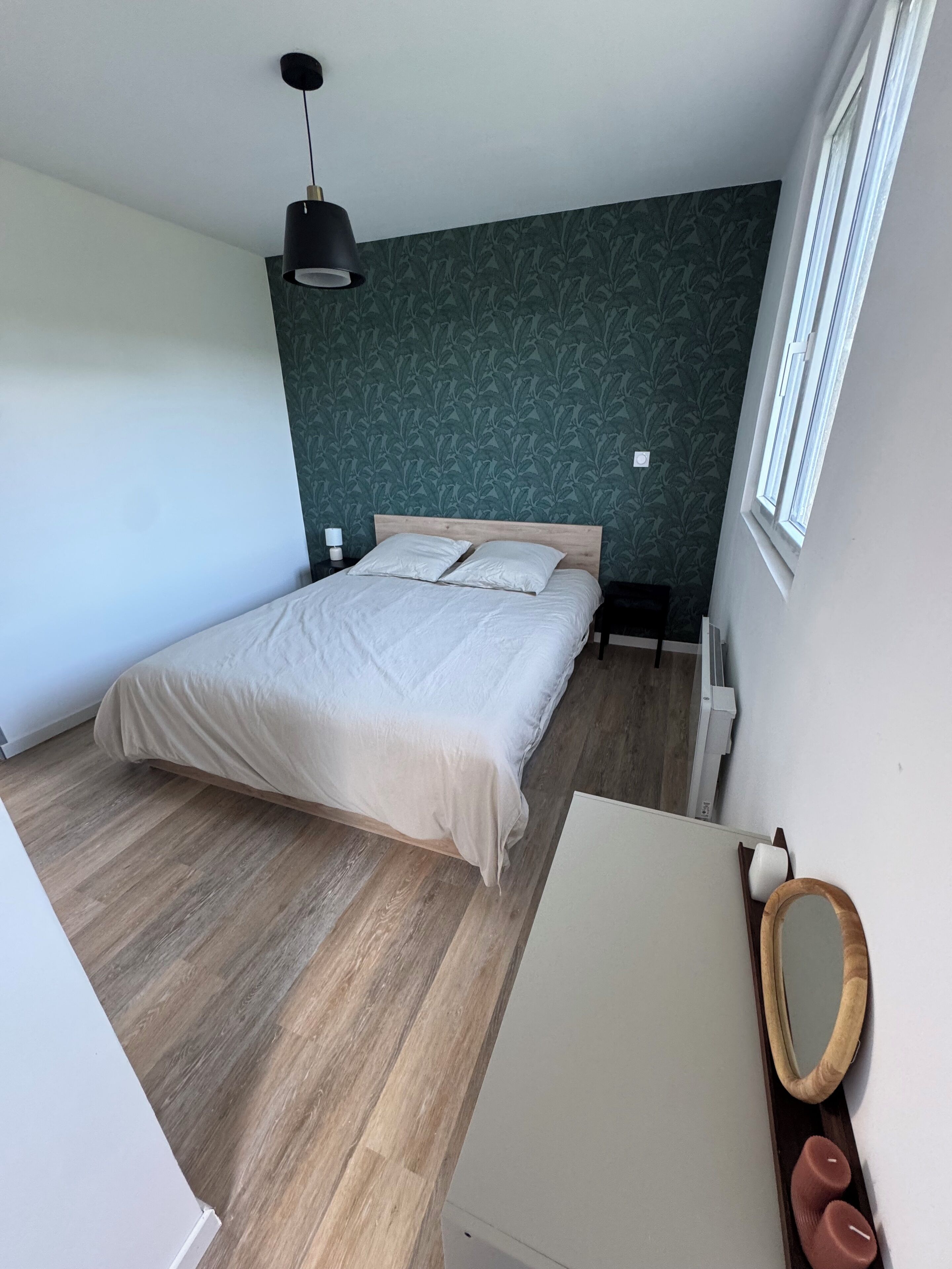 Ein Schlafzimmer mit einem großen Bett, Holzboden, einer Wand mit grünem Muster, einer Hängelampe und einem Fenster.