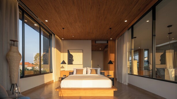 Un dormitorio moderno con una cama grande, techo de madera, ventanas amplias y vistas al exterior.