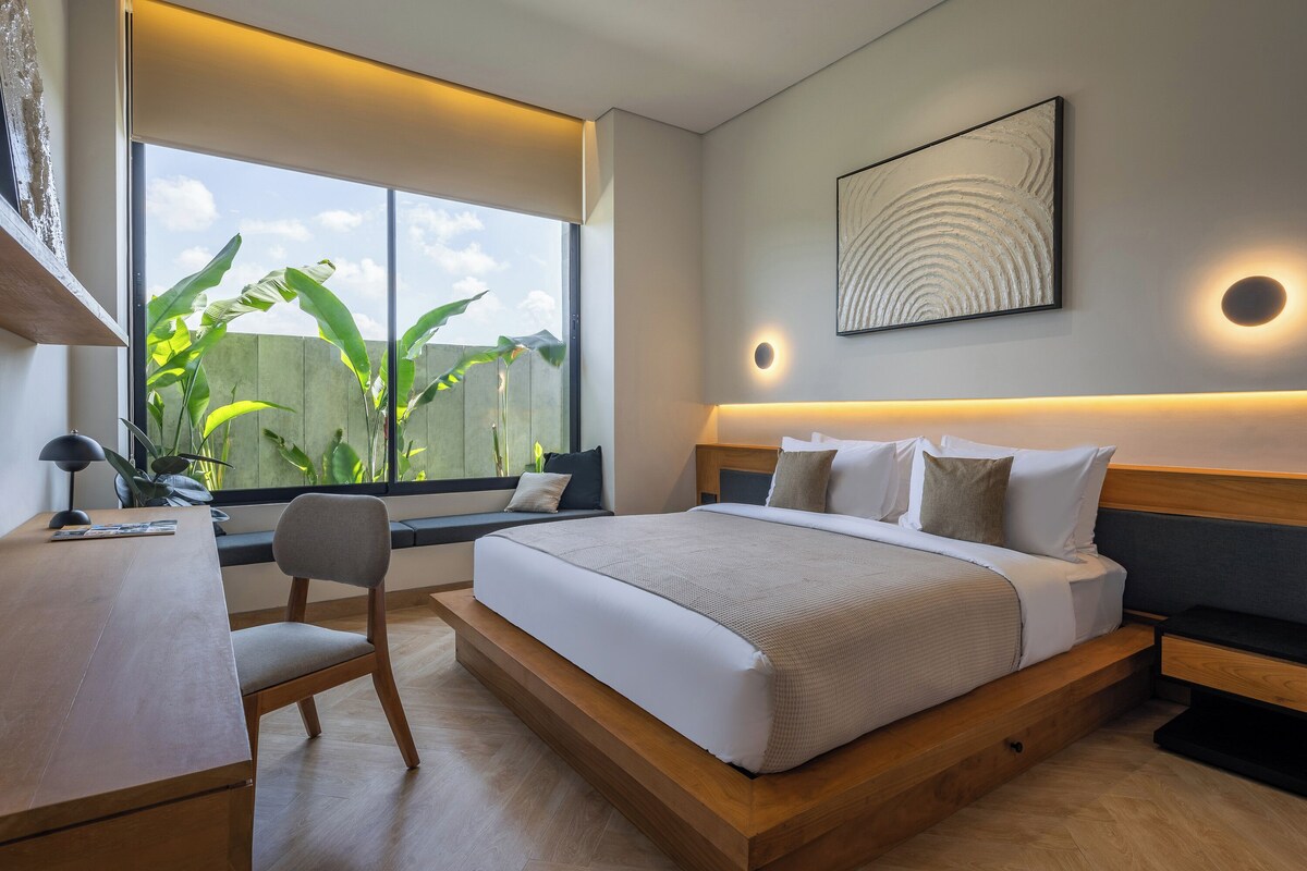 Ein modernes Schlafzimmer mit einem großen Bett, einem Schreibtisch und einem Fenster mit Blick auf Grünflächen.