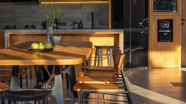 A modern kitchen with wooden cabinetry, a central island with stools, and a dining table. - OASI House Canggu by Nagisa Bali (Canggu)