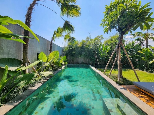 Ein rechteckiger Pool mit klarem Wasser, umgeben von üppiger tropischer Vegetation und einer Holzterrasse.