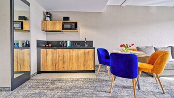 Cocina moderna con armarios de madera, microondas y cafetera. Cuenta con una zona de comedor con mesa, sillas y sofá.