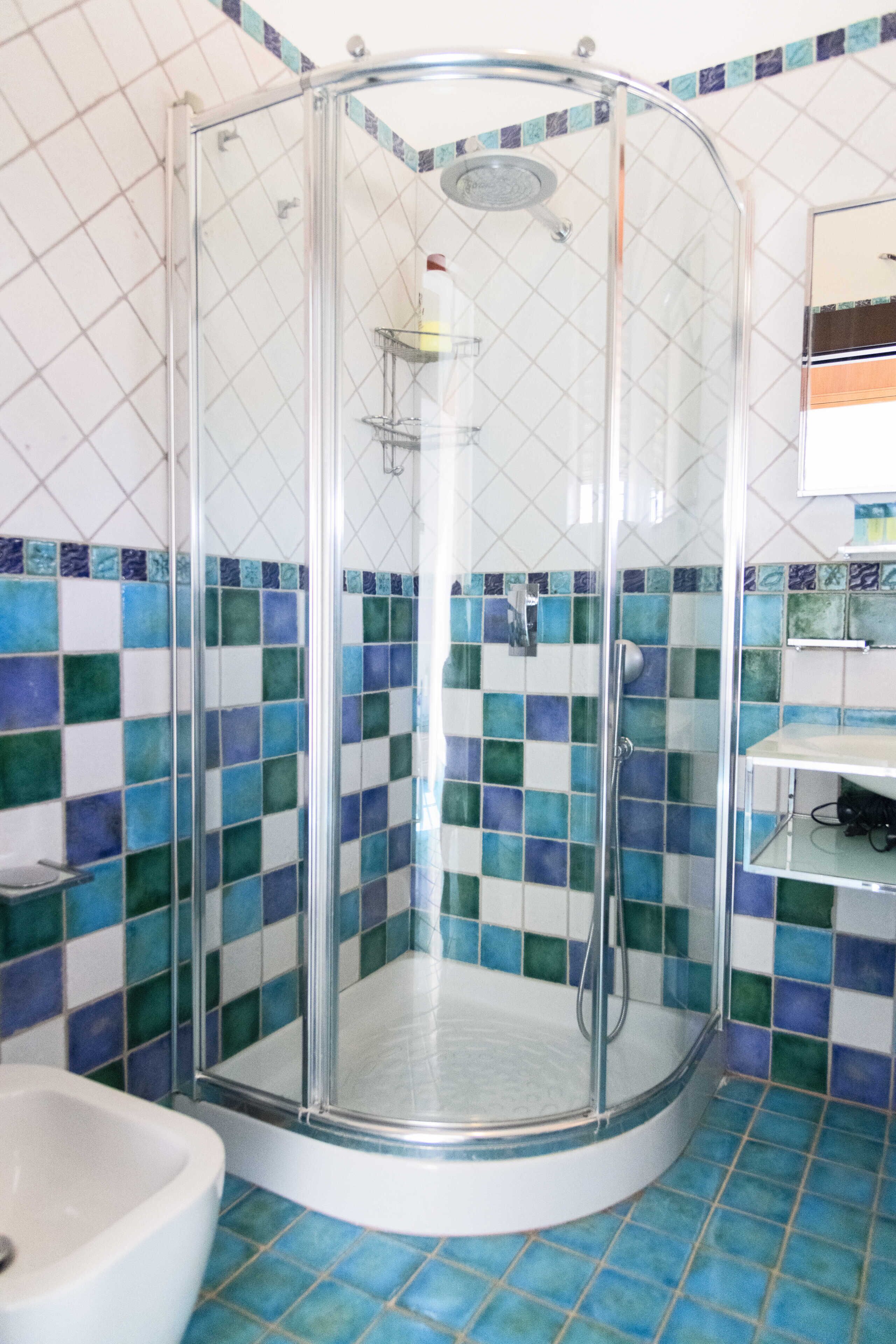 Un box de ducha con paredes de vidrio, piso y paredes de azulejos blancos, un cabezal de ducha cromado y un estante pequeño con artículos de tocador.