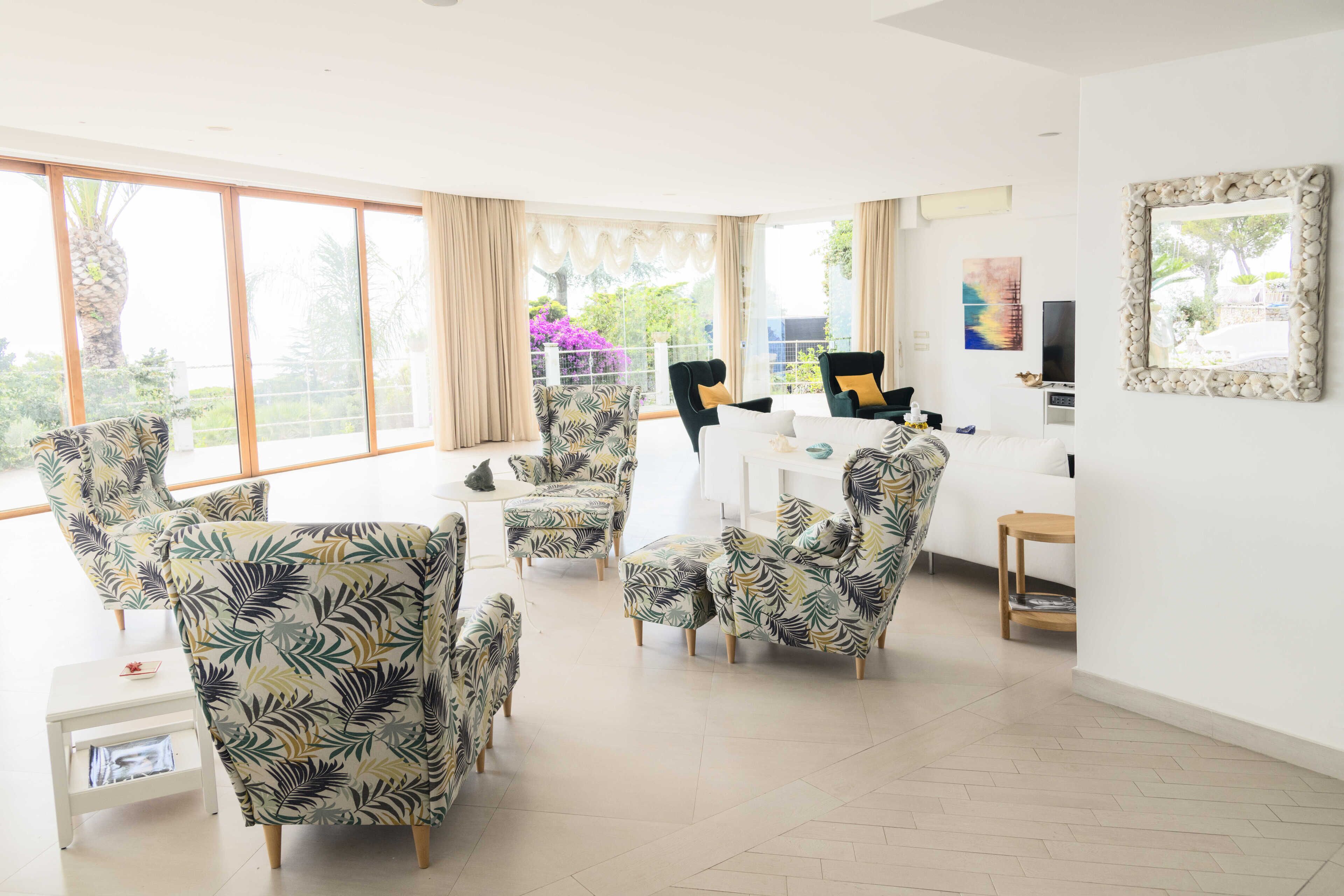 A spacious living room with large windows, a flat-screen TV, and a dining area with a white table and chairs.
