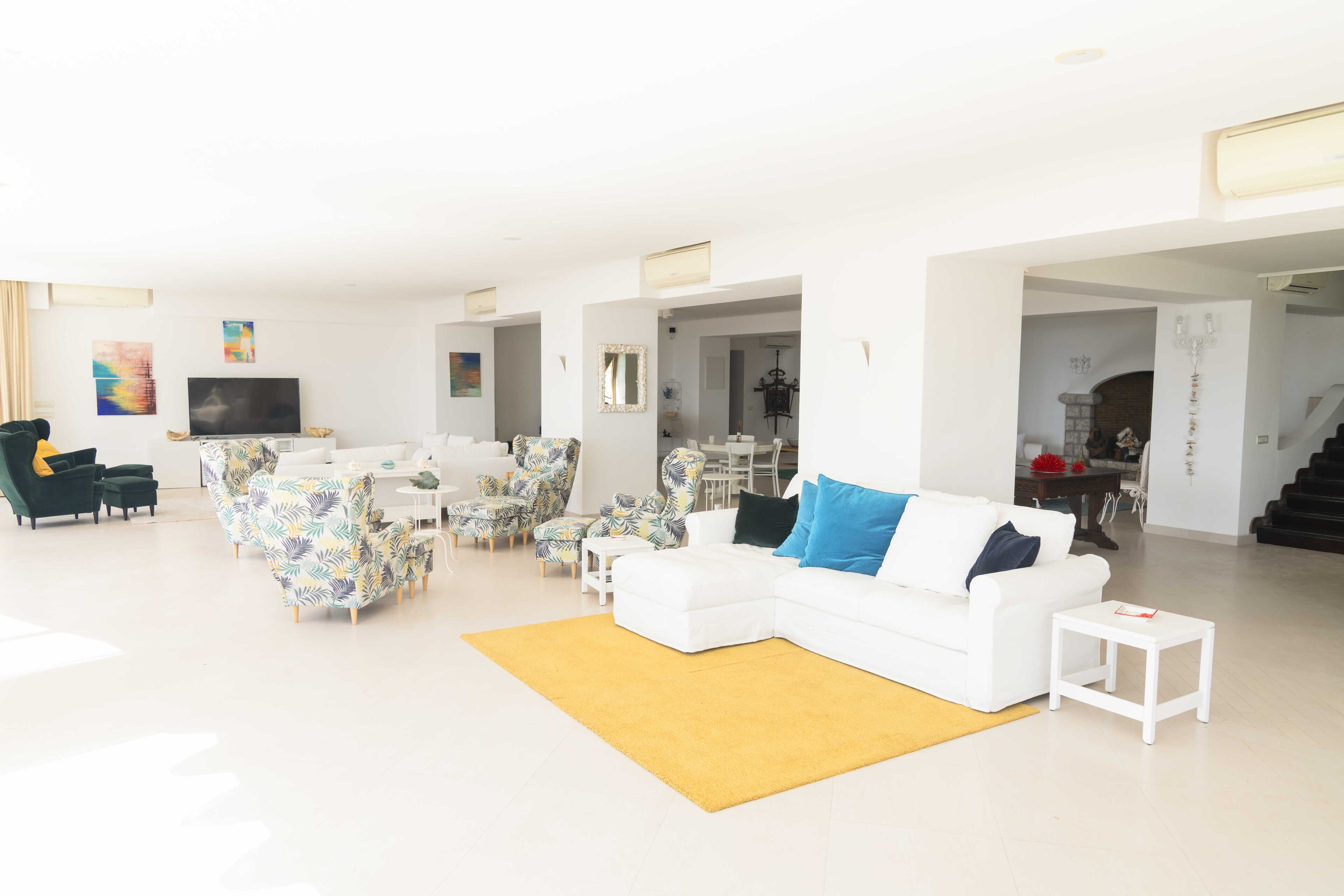 A modern living room with a white sofa, patterned chairs, a yellow rug, and a TV.