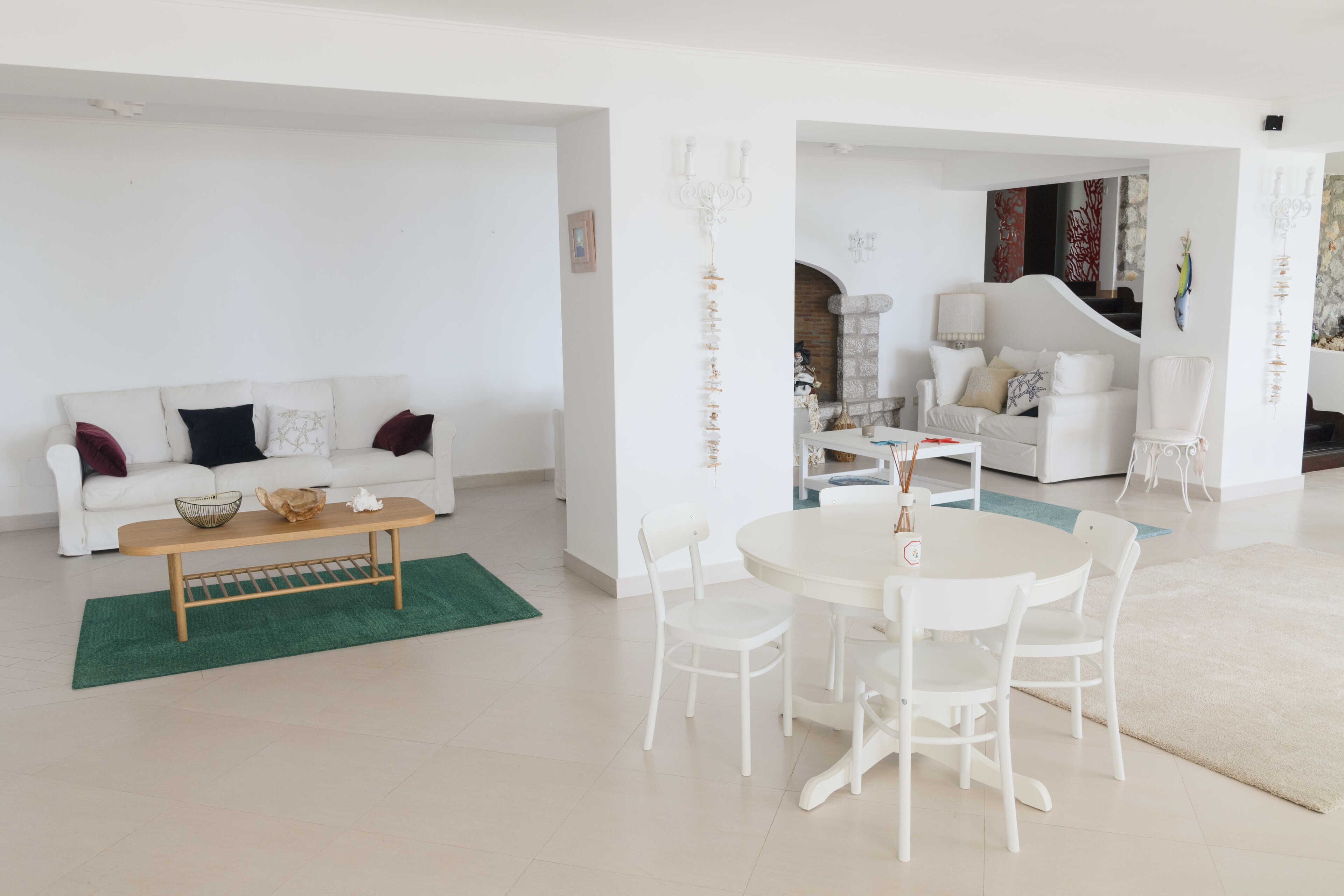 A spacious living area with a white sofa, a round dining table, and white chairs. There is a green rug under the sofa and a white rug under the dining table.