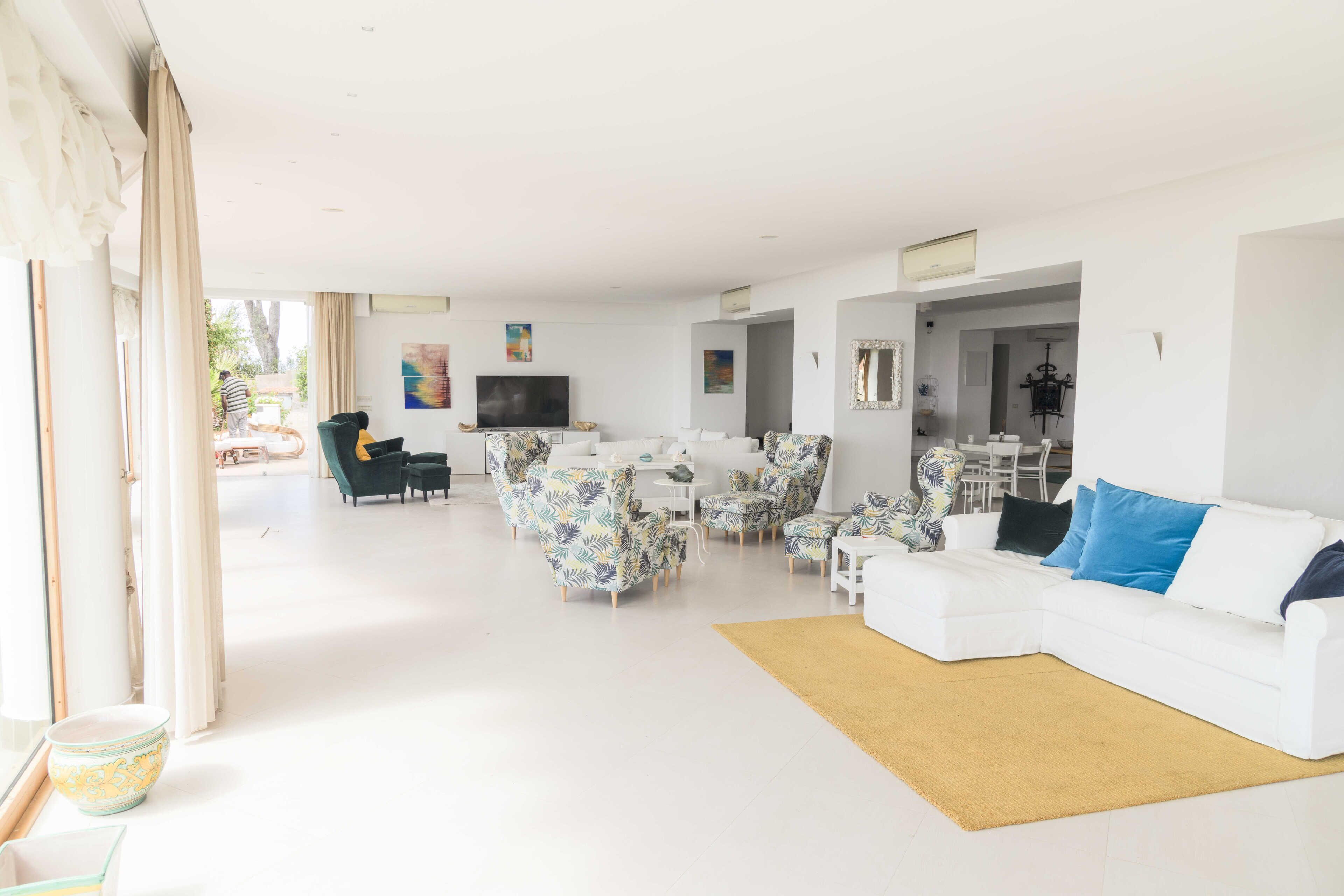 A spacious living room with a white sofa, patterned armchairs, and a television.