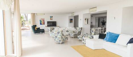A spacious living room with a white sofa, patterned armchairs, and a television.