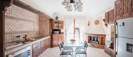 A kitchen with a dining table, cabinets, a refrigerator, and a fireplace.