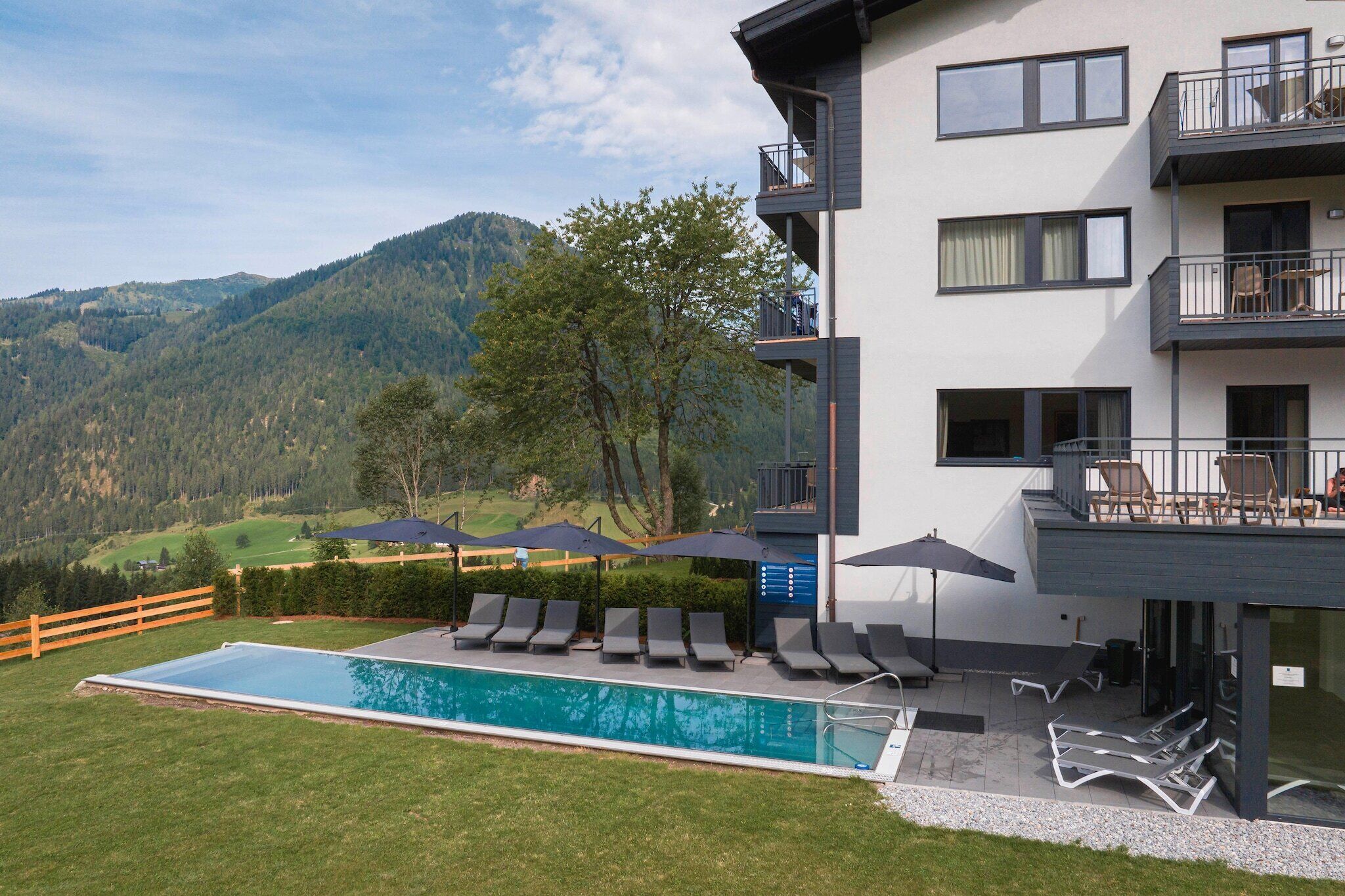 En modern byggnad med pool, utomhusmöbler och utsikt över bergen.