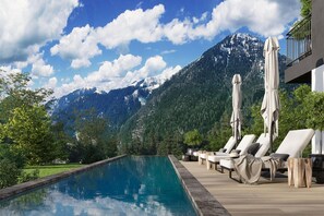 Un espace aménagé au bord de la piscine, avec des chaises longues et des parasols, offrant une vue sur un paysage montagneux.