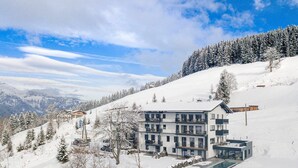 Un hotel moderno a più piani con piscina, circondato da alberi e montagne innevate.