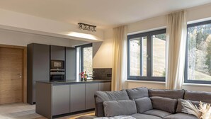 Una cucina moderna con forno integrato e microonde, un divano grigio e un'ampia finestra con tende.