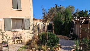 Une cour avec un chemin en pierre, des plantes en pot, un banc en bois et une échelle.