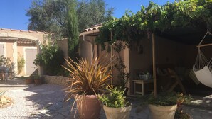 Une cour agrémentée de plantes en pot, d’une chaise suspendue et d’un bâtiment rustique surmonté d’un toit en tuiles.