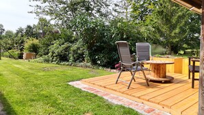A wooden deck with a round table and two chairs, surrounded by a well-maintained lawn and dense foliage. - Fewo zum Königreich.... where others go on vacation  (Westerwalsede)