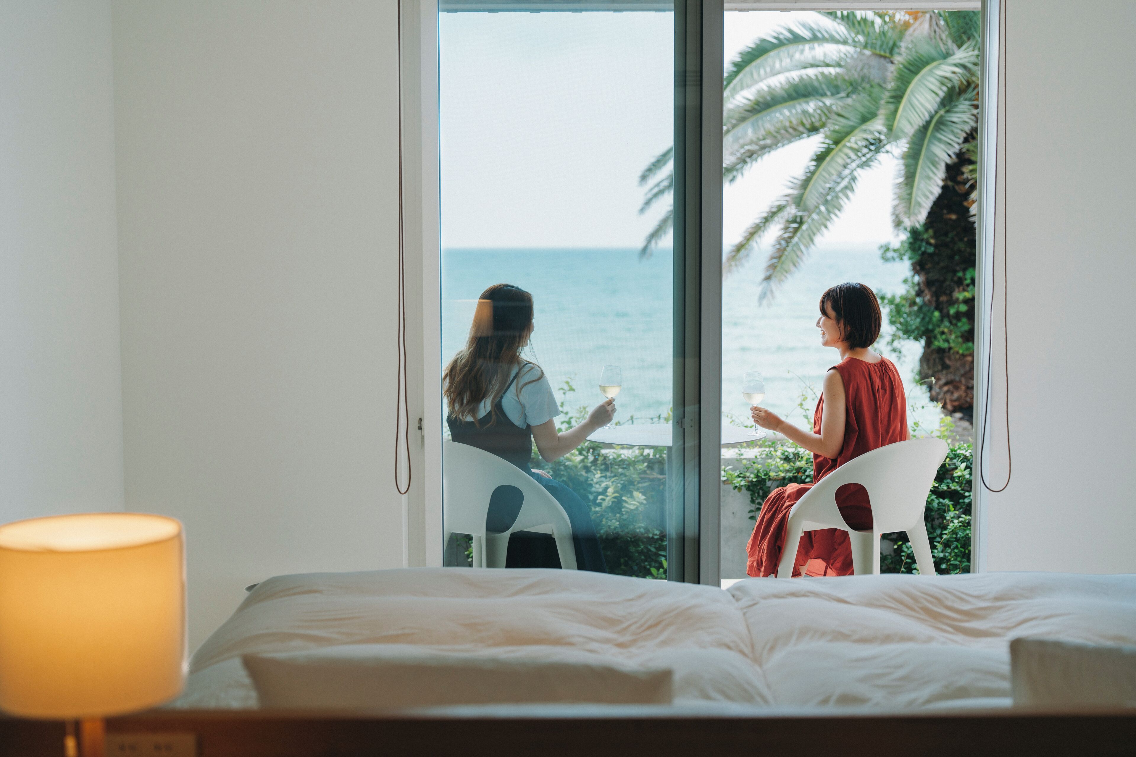 Una habitación con cama, lámpara y vista al mar a través de un ventanal corredera.