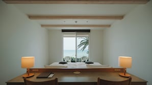 A room with a bed, two chairs, a desk, and a window with a view of the ocean. - Colorit GOTO ISLANDS (Goto)
