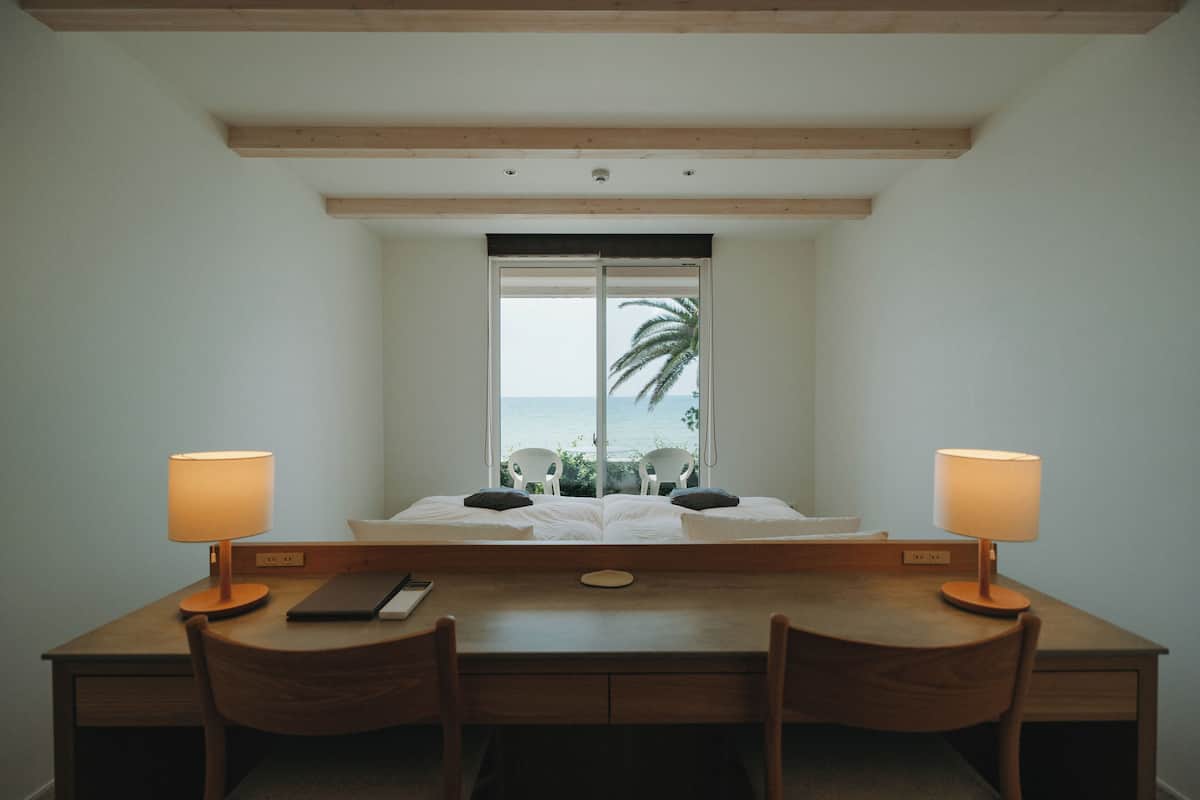 Una habitación con una cama, dos sillas, un escritorio y una ventana con vista al océano.