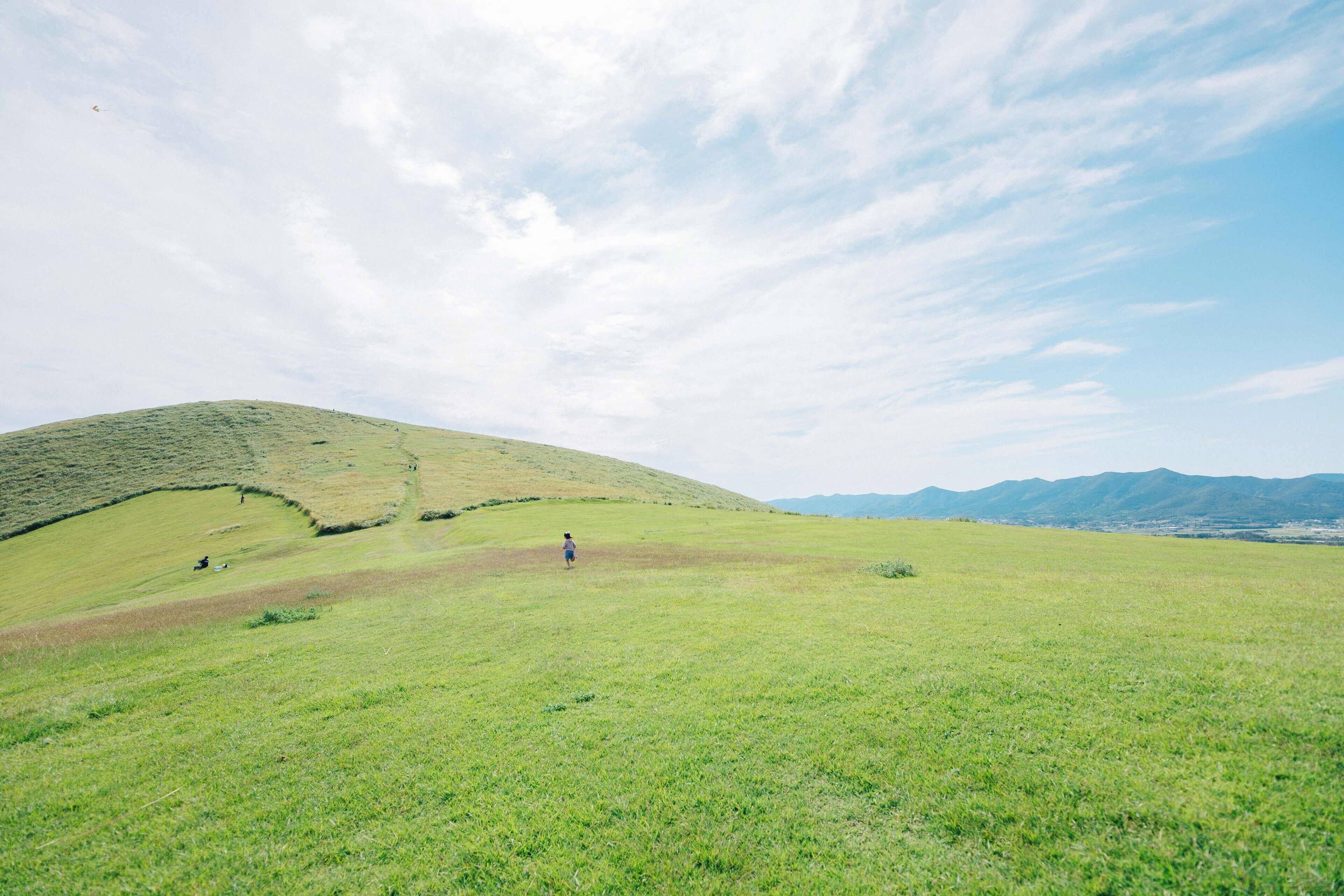 Ein grünes Feld mit einem Hügel und Bergen im Hintergrund.