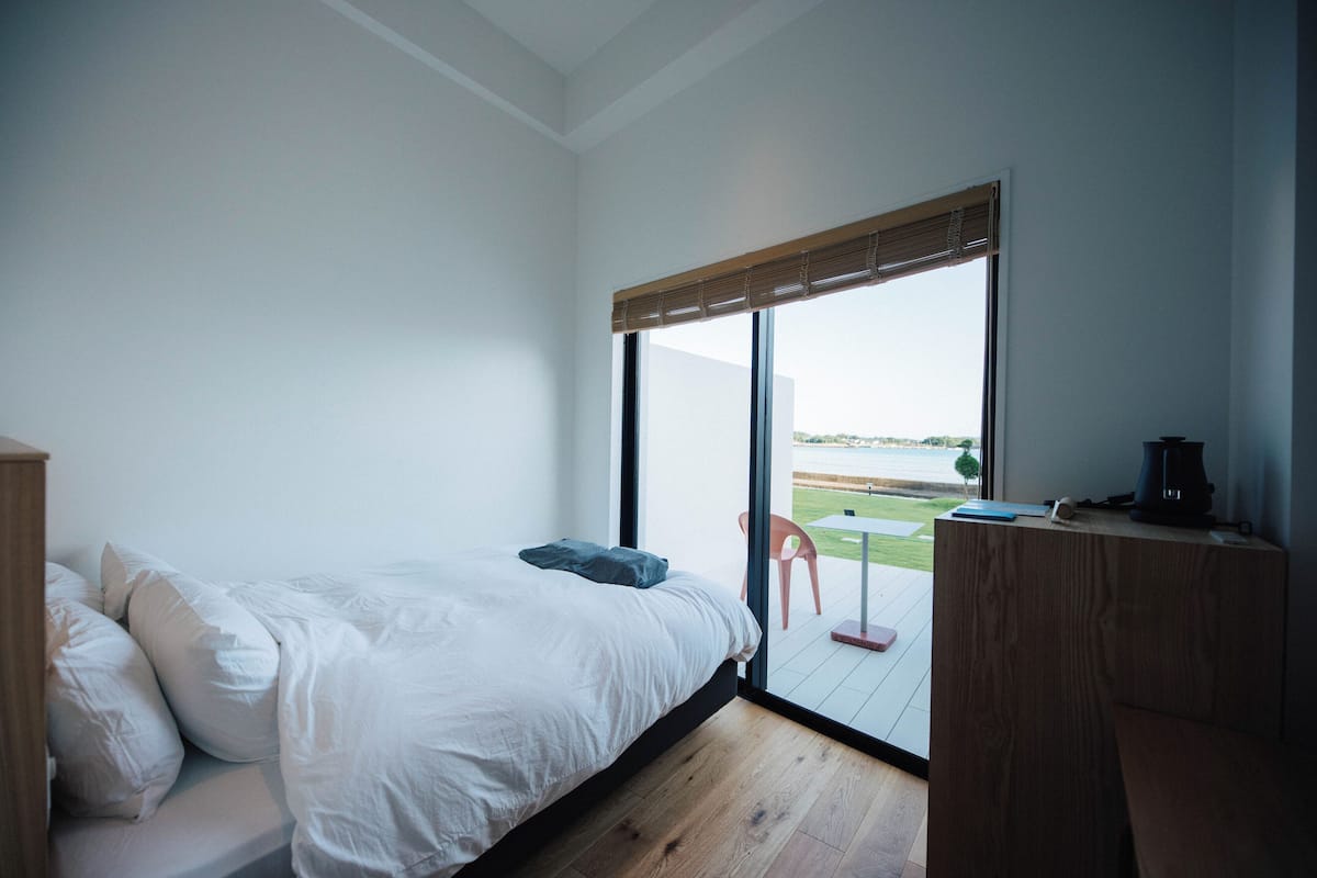Un dormitorio con un ventanal grande, una cama, un escritorio de madera y vistas al exterior.