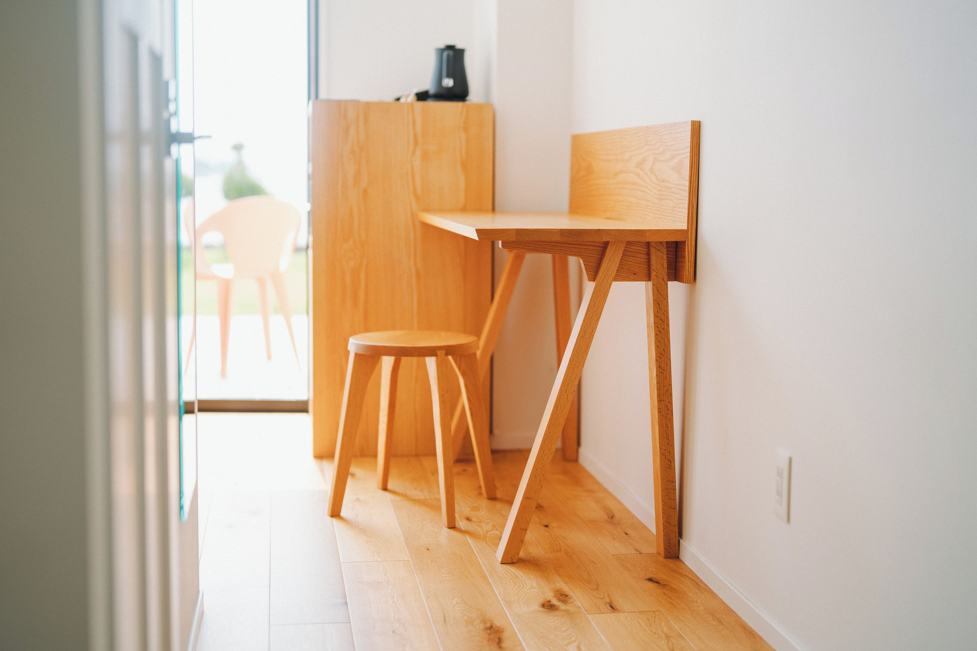 A wooden desk and chair in a bright room with a view of the outdoors.