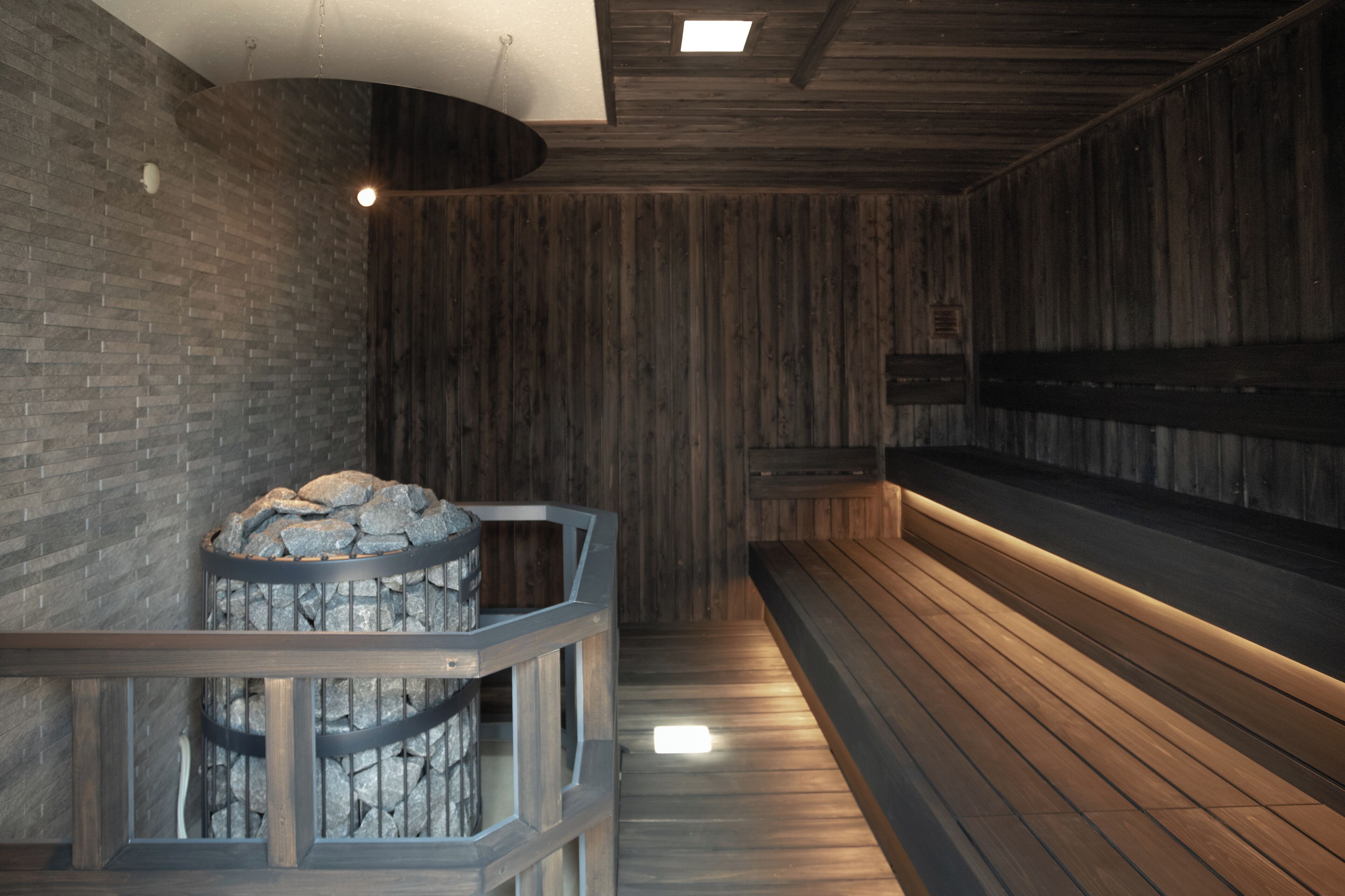A sauna with wooden walls and benches, a stone feature, and a ceiling light.