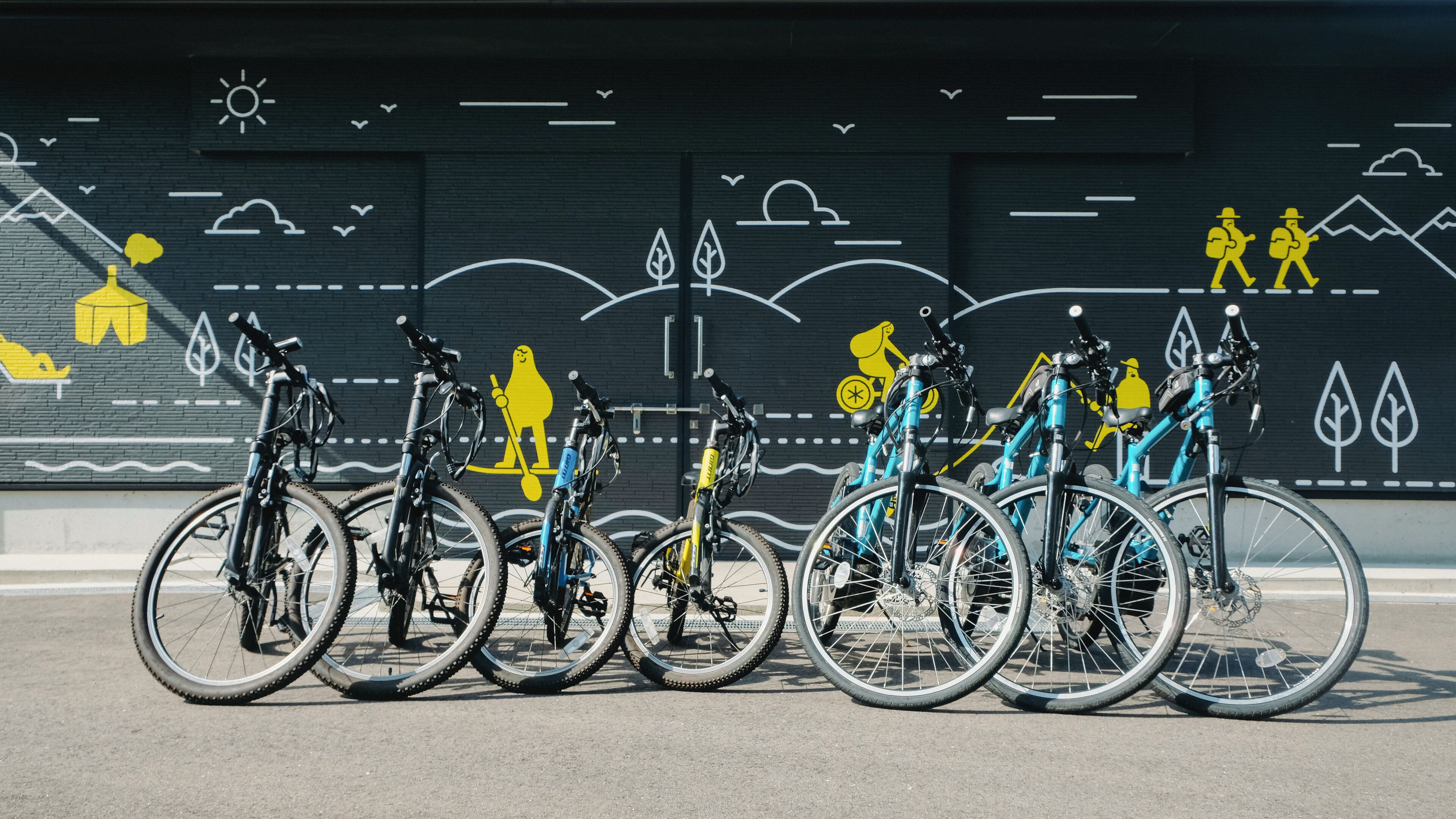 A row of bicycles parked in front of a mural with various outdoor scenes.