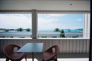 Ein Balkon mit Tisch und zwei Stühlen, mit Blick auf eine Küstenlandschaft mit Gebäuden und Palmen.