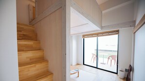 A modern interior with a wooden staircase, a sliding glass door leading to an outdoor area with chairs, and a small table. - Colorit GOTO ISLANDS (Goto)