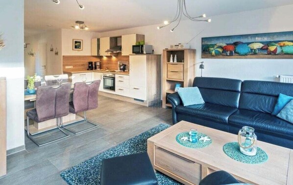 Un salon moderne avec un canapé en cuir noir, une table basse en bois et un coin repas comprenant un tabouret de bar et des chaises.