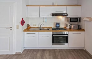 Uma cozinha compacta com armários brancos, bancada de madeira, forno de aço inoxidável, micro-ondas e pia.