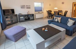 Uma sala de estar moderna com um sofá, uma mesa de centro, uma televisão e um espaço de jantar com cadeiras e uma mesa.