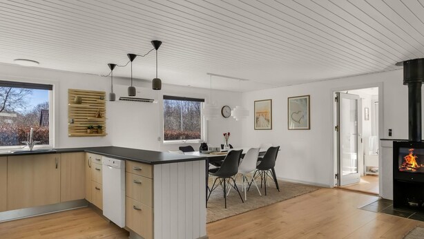 Una cocina moderna con una isla central, comedor con sillas, chimenea y ventanas amplias.