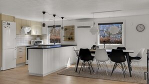 Una cocina moderna con armarios blancos, una isla central, iluminación colgante y un comedor con mesa y sillas.