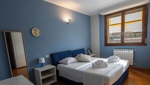 Quarto com cama, mesas de cabeceira, luminária, espelho, janela e radiador.
