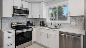 Eine moderne Küche mit weißen Schränken, einer Edelstahl-Mikrowelle, einem Backofen, einem Geschirrspüler und einem Fenster mit Blick nach draußen.