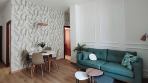 Una sala de estar moderna con un sofá verde, una mesa de comedor con sillas y un papel tapiz estampado.