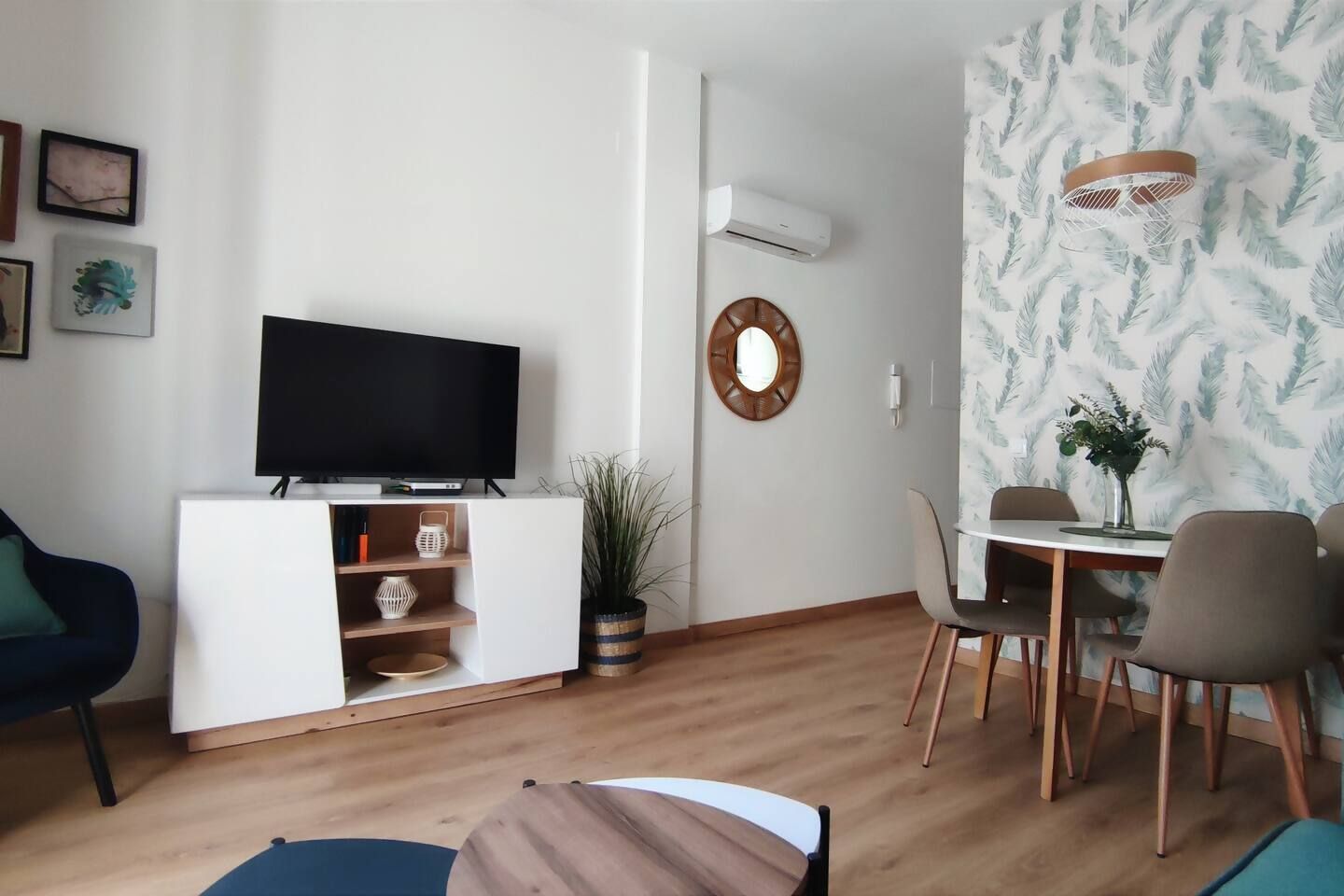 Un salon moderne doté d’un téléviseur à écran plat, d’un coin repas avec une table et des chaises, d’une plante en pot et d’un climatiseur fixé au mur.
