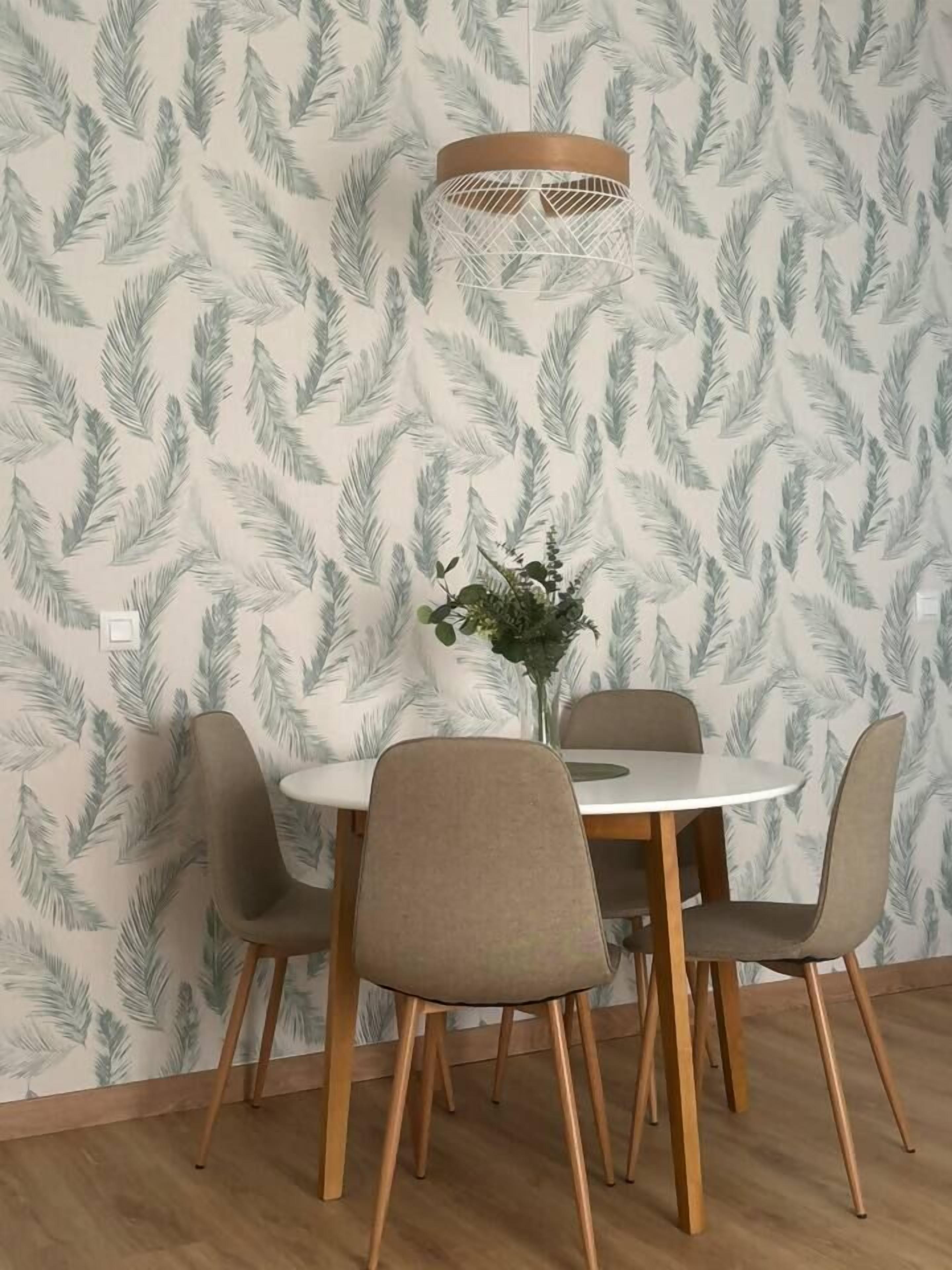 Un comedor con una mesa redonda y cuatro sillas, un jarrón con flores, y una pared con un diseño de hojas.