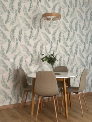 A dining area with a round table and four chairs, a vase with flowers, and a wall with a leaf pattern. - Casa Yaye Puerta Palma (Écija)