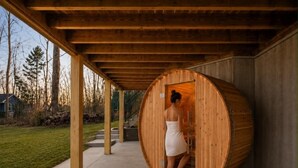 A sauna with a wooden exterior, a covered walkway, and a view of a residential area with trees and a house. - Luxurious 8-Bed Lakefront Retreat with Private Beach, Hot Tub & Sauna! (Bumpass)