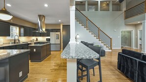 A modern kitchen with granite countertops, a central island, and a staircase leading to an upper level. - Luxurious 8-Bed Lakefront Retreat with Private Beach, Hot Tub & Sauna! (Bumpass)