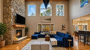A spacious living room with a stone fireplace, a large sectional sofa, and a flat-screen TV mounted on the wall. - Luxurious 8-Bed Lakefront Retreat with Private Beach, Hot Tub & Sauna! (Bumpass)