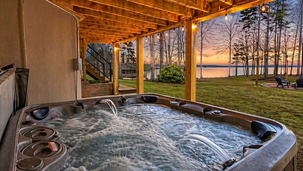 A hot tub under a wooden pergola with a view of a lake and trees at sunset. - Luxurious 8-Bed Lakefront Retreat with Private Beach, Hot Tub & Sauna! (Bumpass)