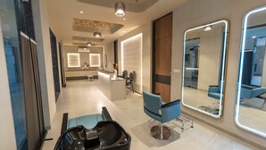 A modern hair salon interior with a reception desk, a blue salon chair, and a large mirror with a lighted frame. - FULLY FURNISHED STUDIO APARTMENT WITH   BALCONY,  (Vadodara)