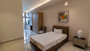 A modern hotel room with a bed, bedside table, and a painting on the wall. - FULLY FURNISHED STUDIO APARTMENT WITH   BALCONY,  (Vadodara)