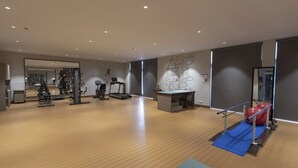 A spacious gym with exercise equipment, a mirrored wall, and a desk area. - FULLY FURNISHED STUDIO APARTMENT WITH   BALCONY,  (Vadodara)