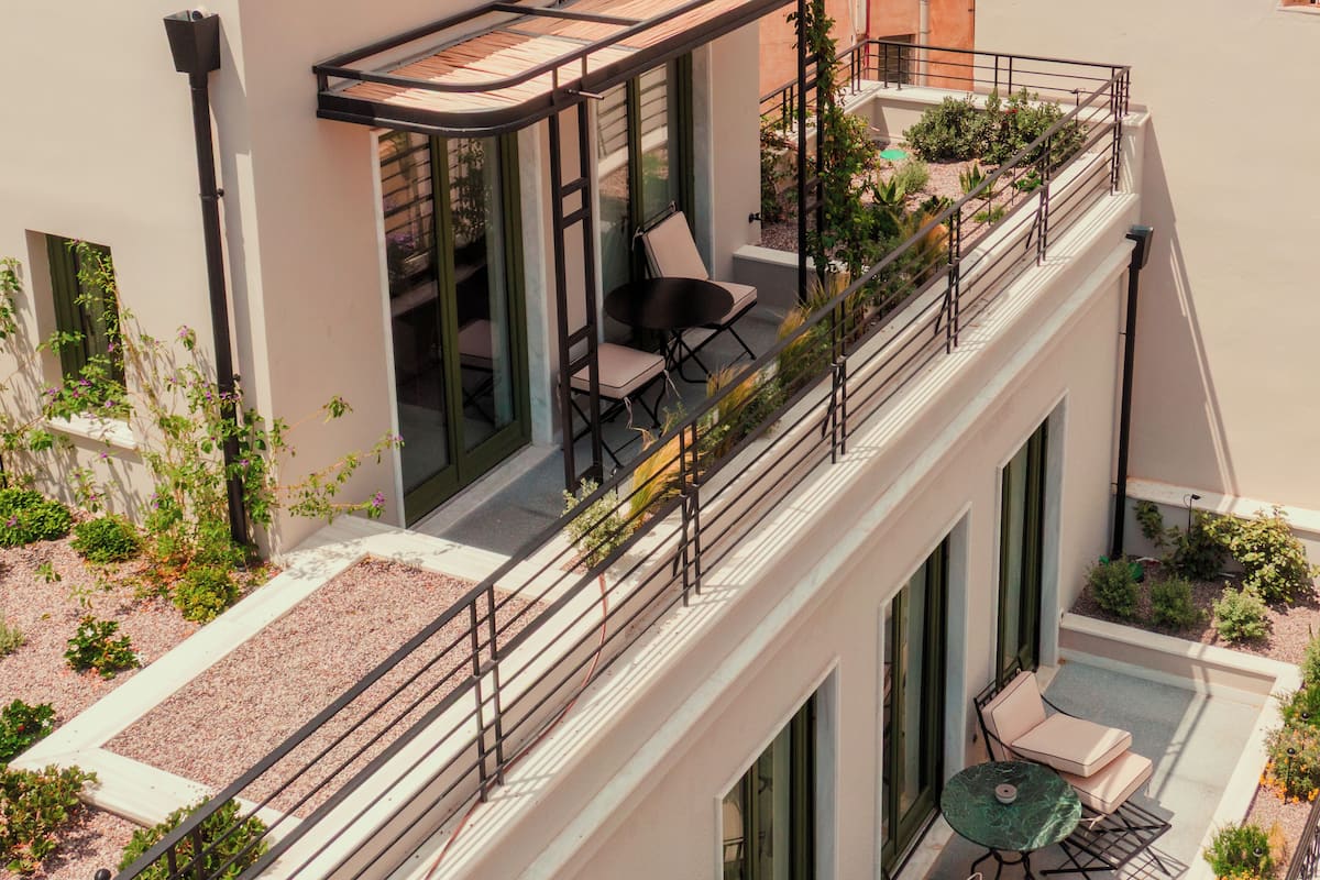 A modern building with a balcony featuring outdoor seating, a pergola, and a garden area.